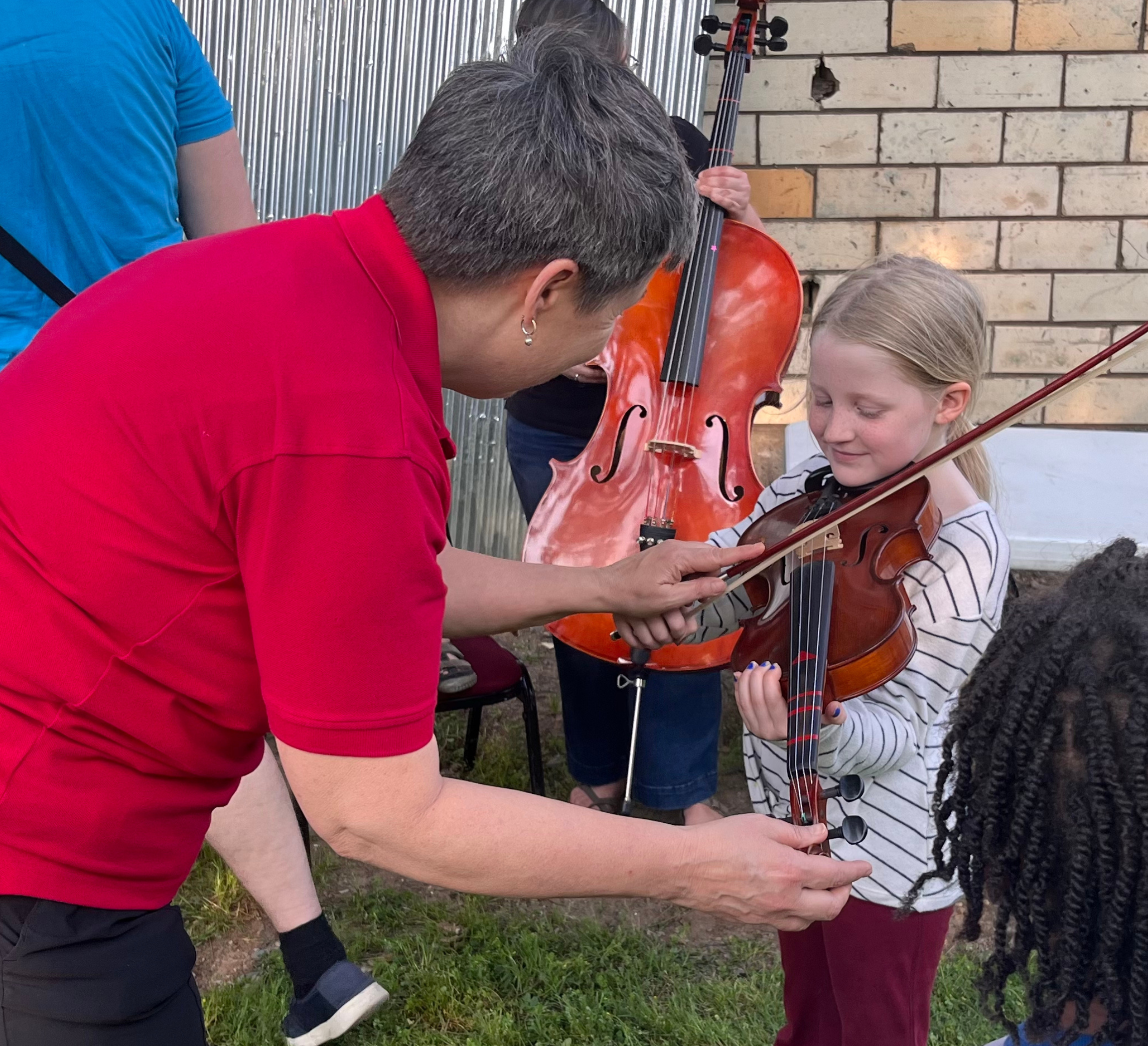 woman in red shirt assists young child with a violin